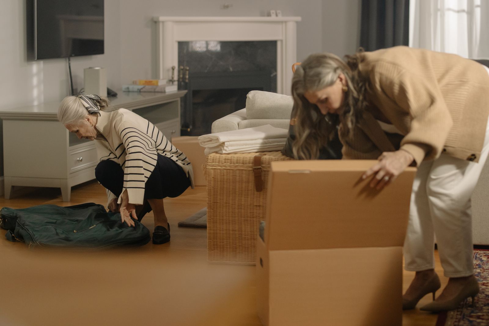 Zwei ältere Frauen packen in einem Wohnzimmer gemeinsam Umzugskartons und Taschen
