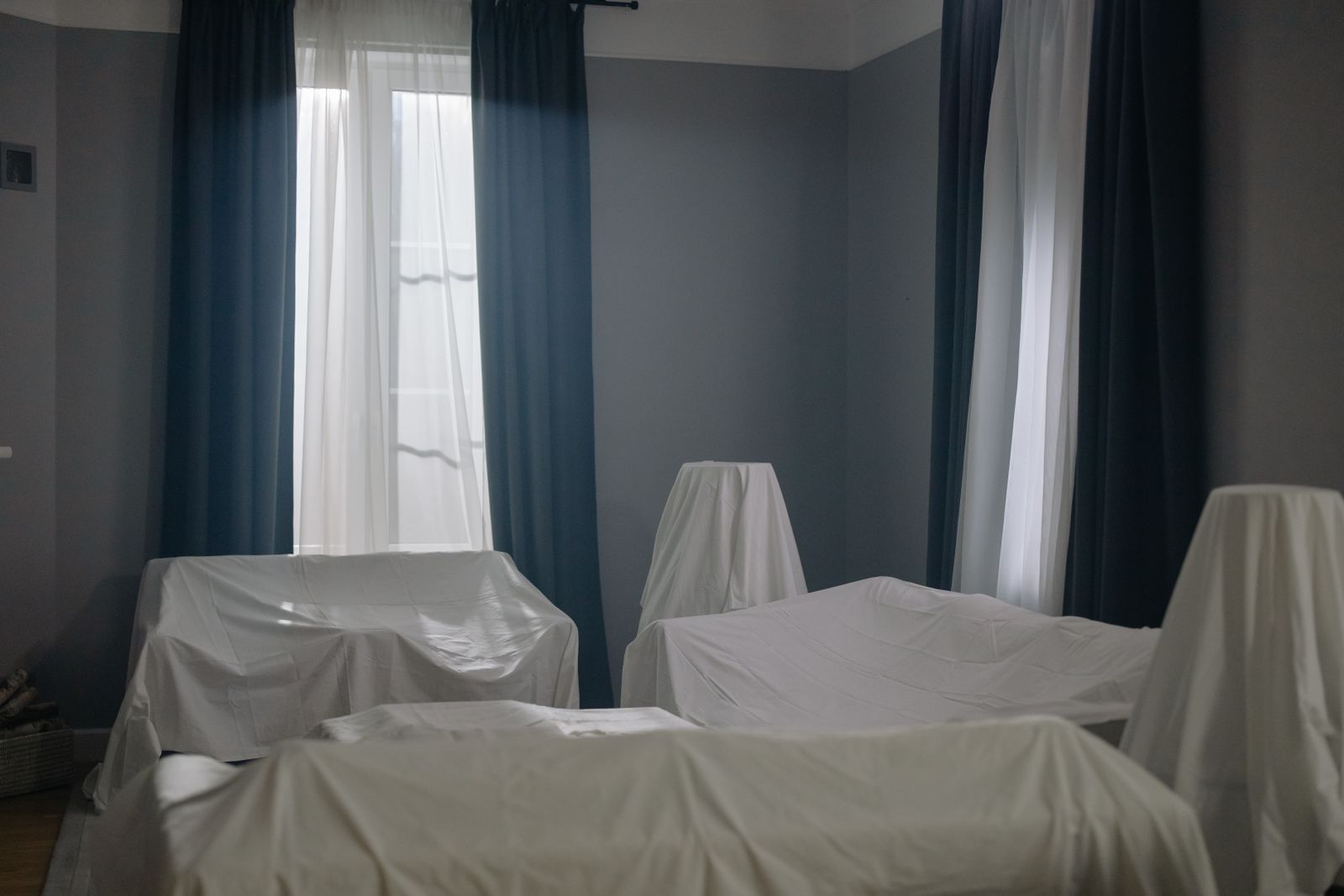 Wohnzimmer mit Sofa, Sessel und Tisch, alle Möbel sind mit weißen Tüchern abgedeckt