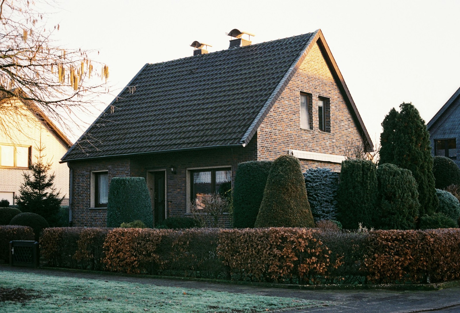 Freistehendes Klinker-Einfamilienhaus hinter einer Buchenhecke, die Fenster sind verhängt